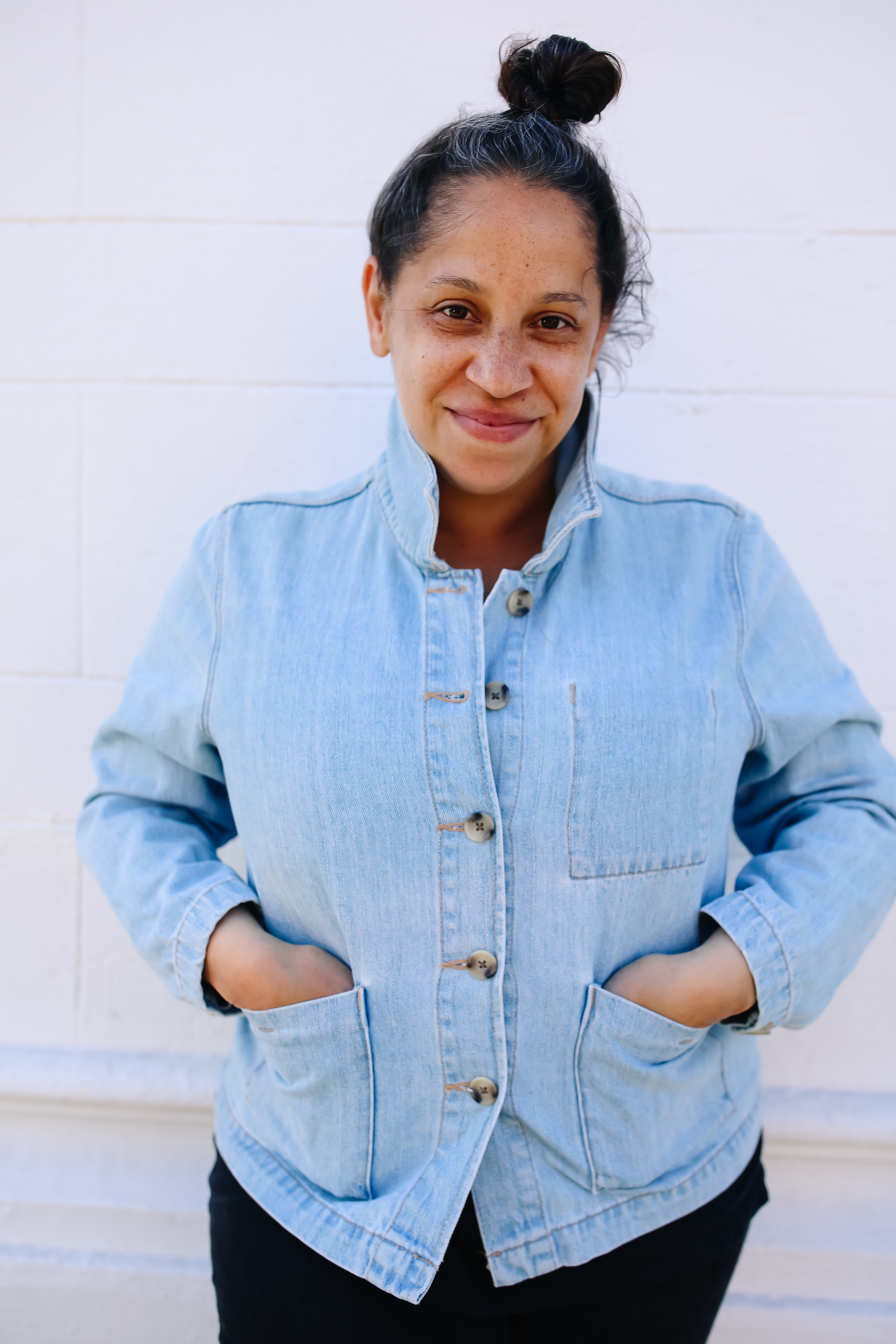 Photo of Luisa Alberto, a woman with her hair in a bun on top of her head and wearing a light blue denim jacked with her hands in the front jacket pockets