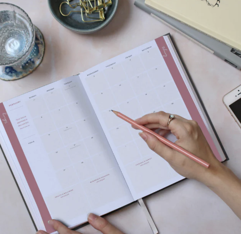 2023 Ponderlily Weekly Planner in rose cover sitting on marble tabletop with paperclips and a gold pen next to it