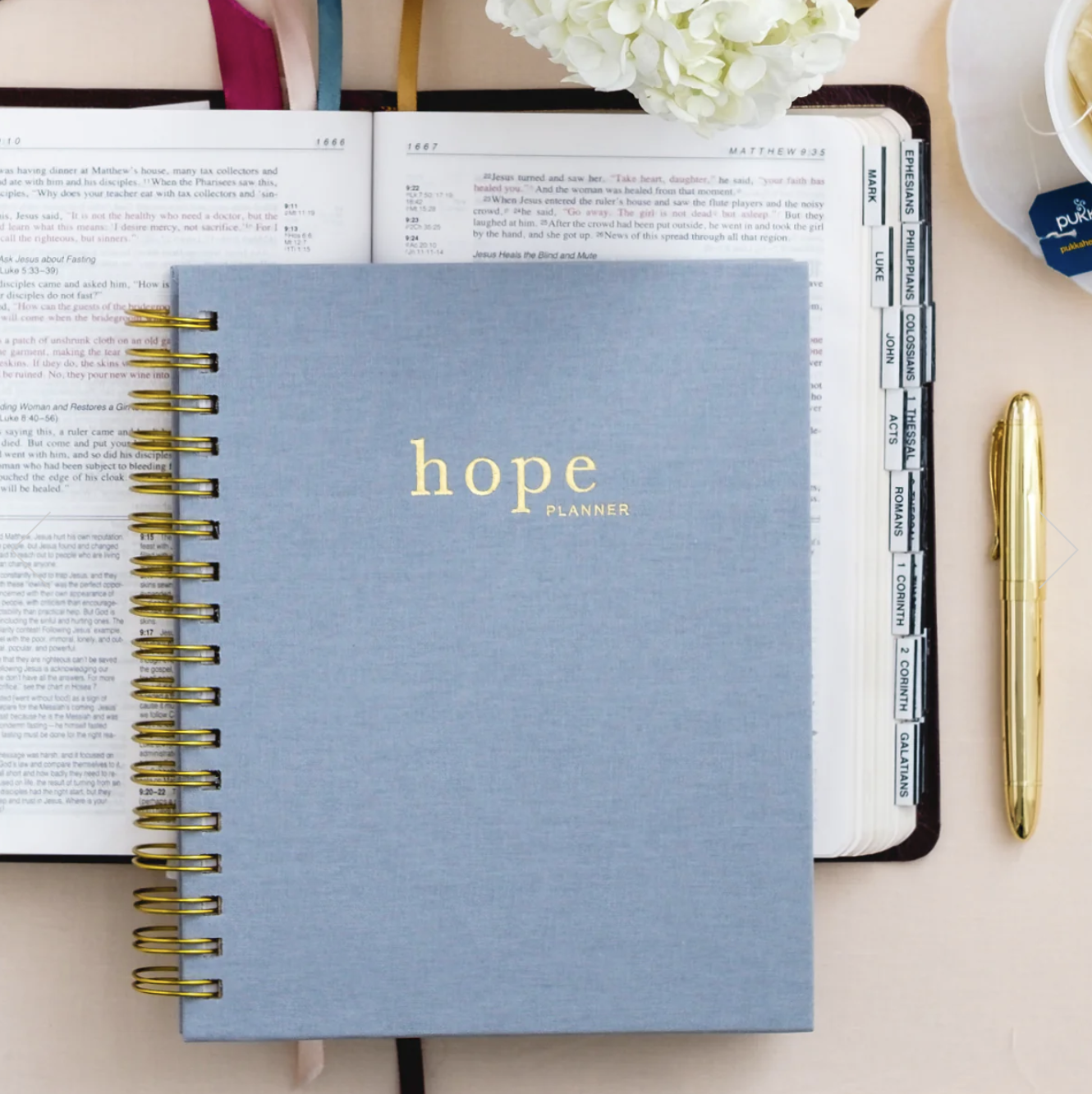 2023 Hope planner with blue spiral-bound cover sitting atop the Bible with a gold pen nearby